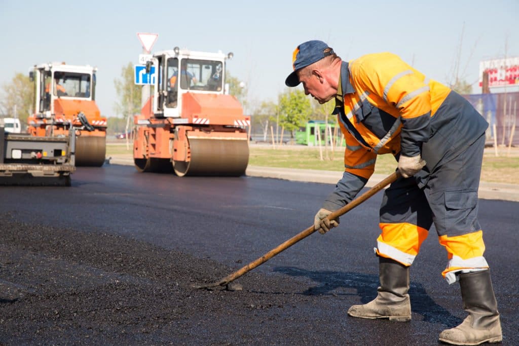 Paving crew spreading fresh asphalt beside a road roller – selling an asphalt paving business in Florida