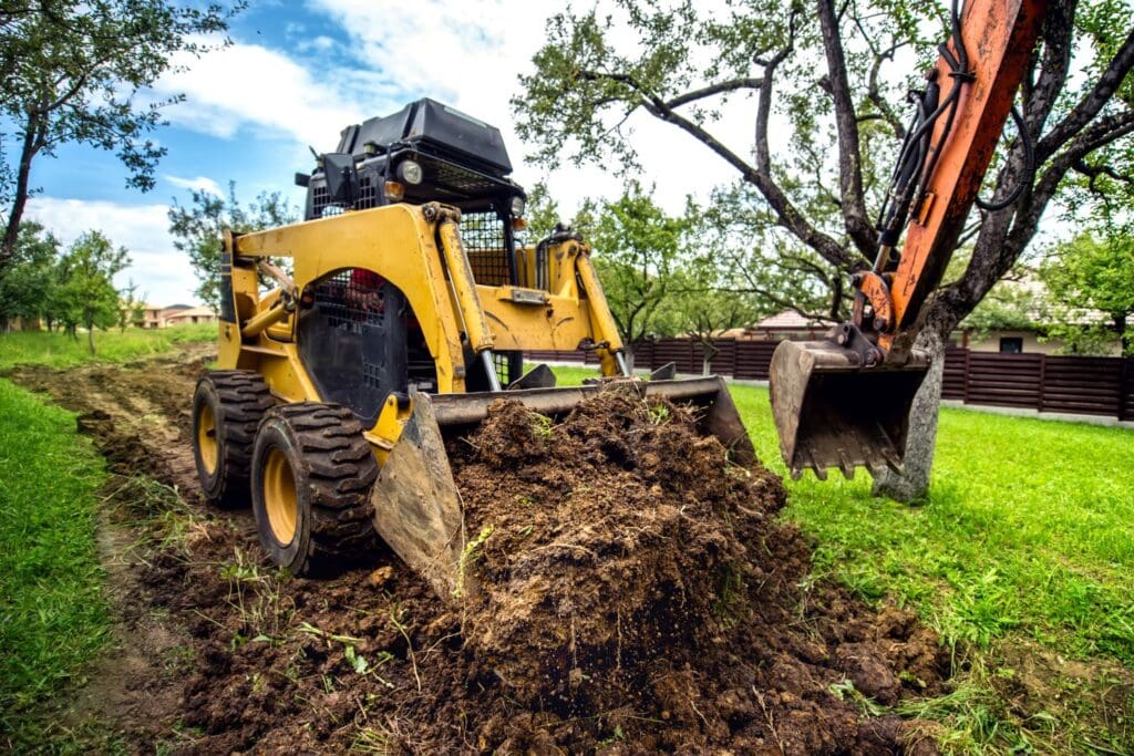 Skid steer grading soil beside an excavator – selling a grading contractor business in Florida