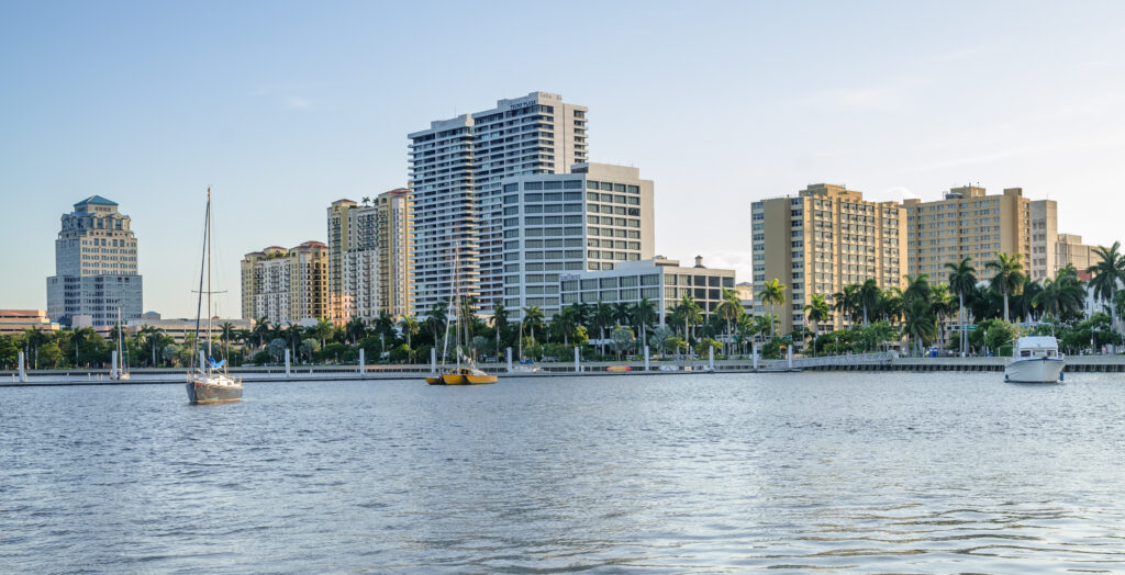Palm Beach Gardens waterfront with high-rise buildings, sailboats, and palm trees, highlighting the area's affluent market and business opportunities.