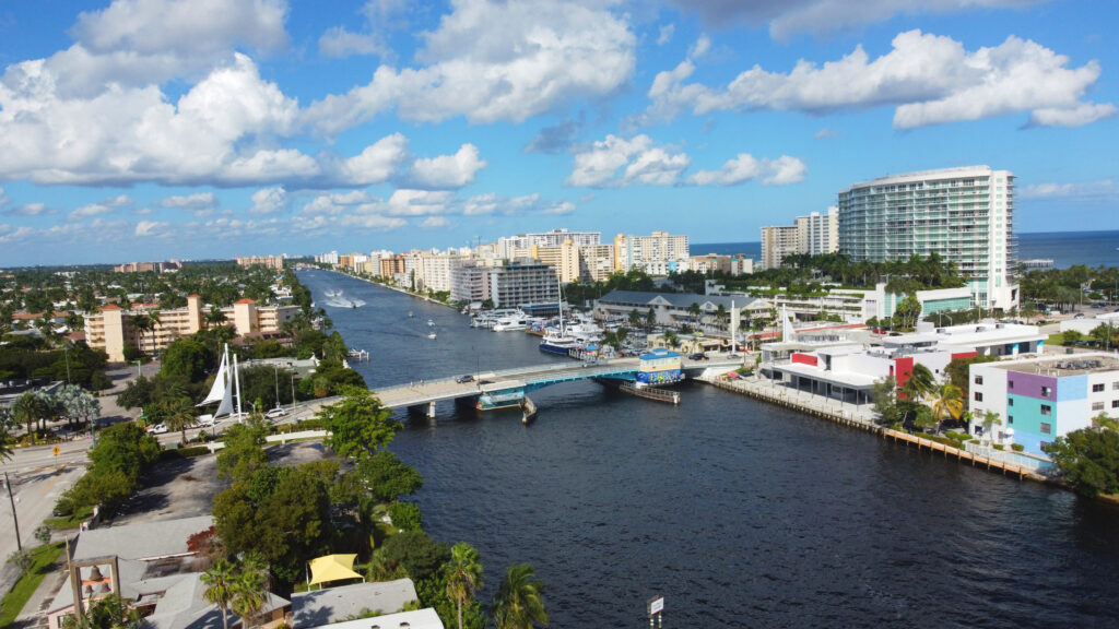 Aerial view of Pompano Beach, Florida, showcasing waterfront properties, boats along the canal, and a vibrant coastal skyline with redevelopment activity.