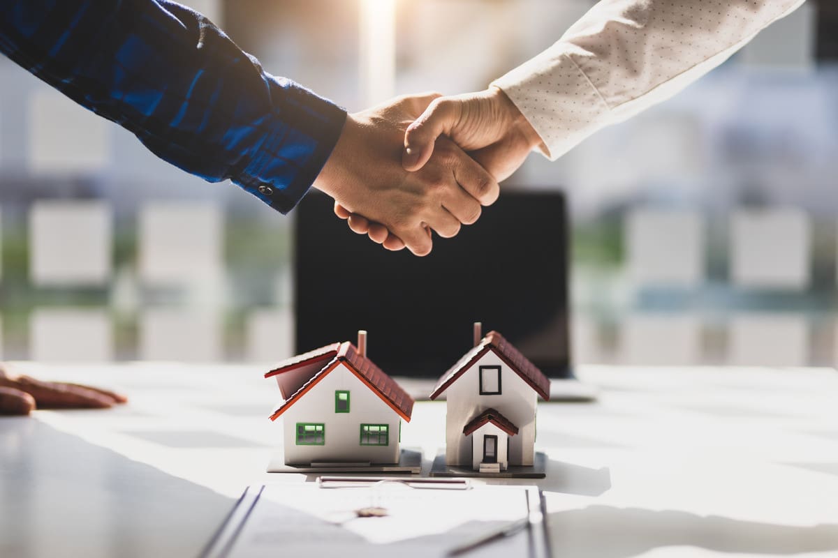 Handshake over a table with miniature house models and blueprints after signing a contract