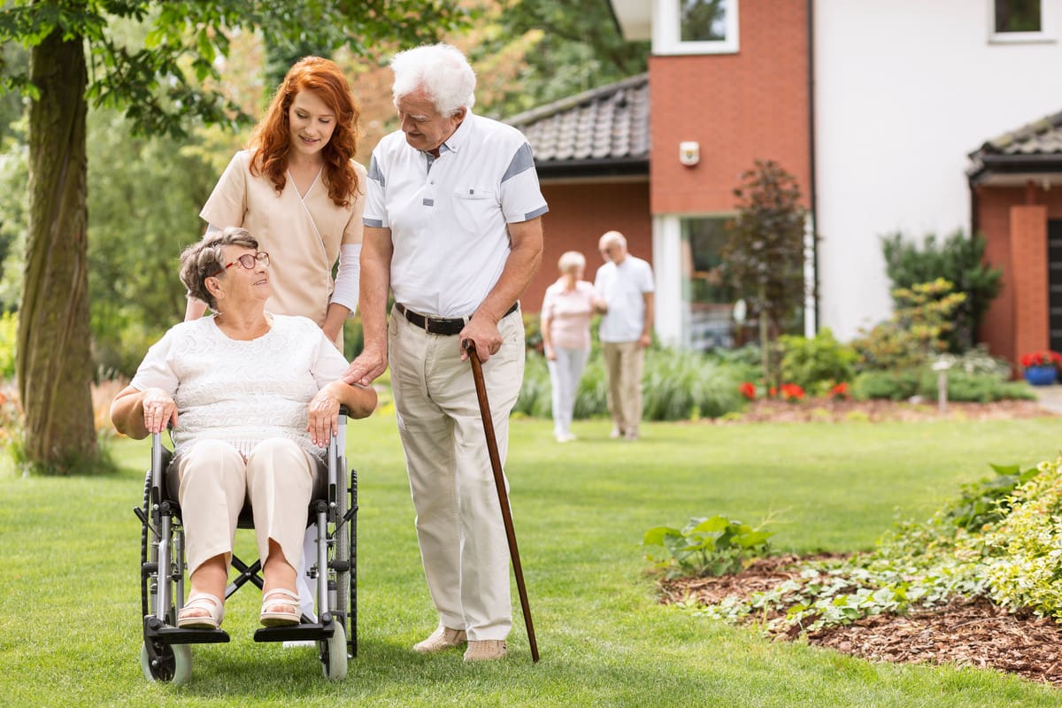 Elderly disabled couple with their caretaker in the garden outside a private rehabilitation clinic