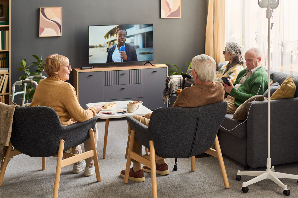 Assisted living facility residents watching television and interacting, illustrating confidentiality during a business sale.